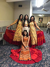 4 Women dressed in traditional outfits of orange and various matching colors.